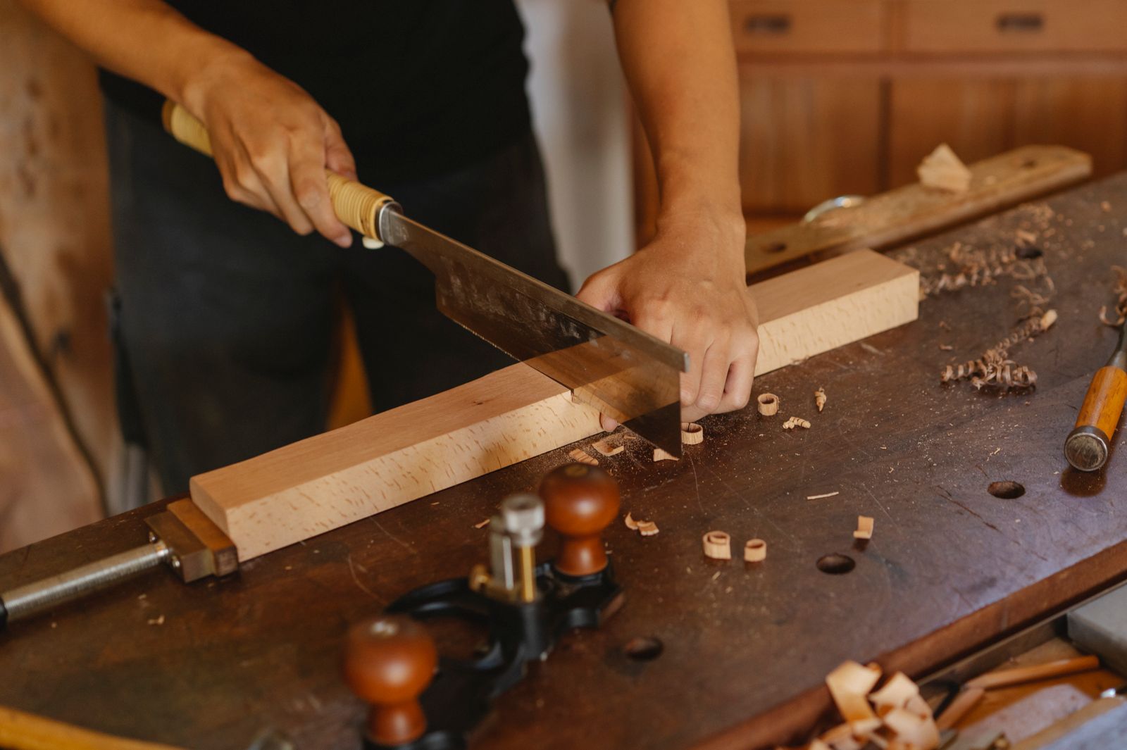 A joiner cutting a plank with a hand saw on a workbench, seen from above