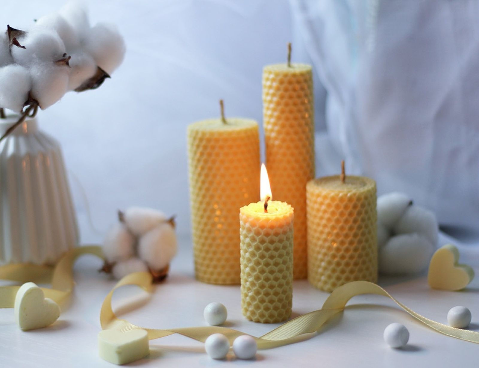 Rolled beeswax candles, one of them lit, on a white table