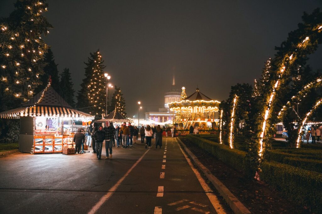 An avenue of Christmas market huts and lit trees at night