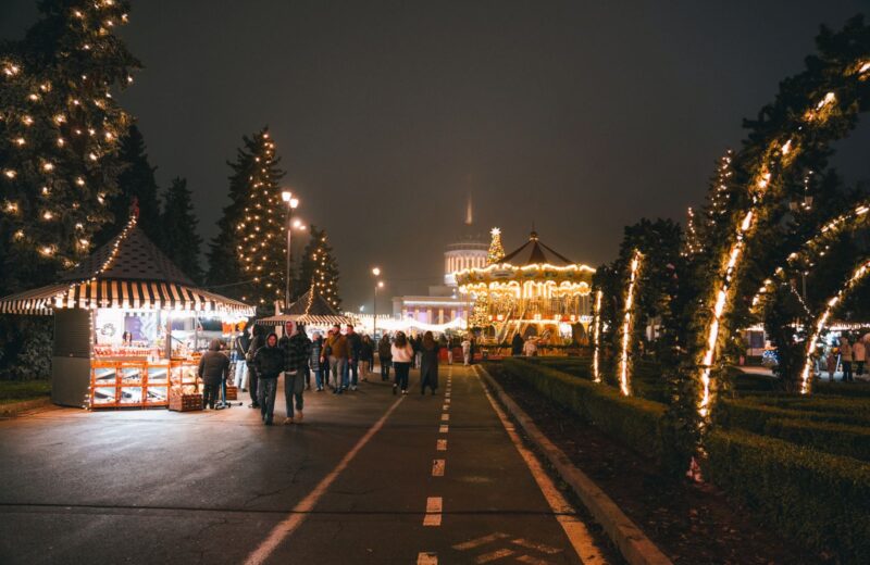 An avenue of Christmas market huts and lit trees at night