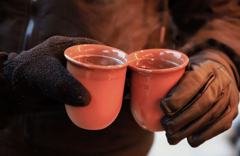 Two people in gloves holding warm mugs at a Christmas market