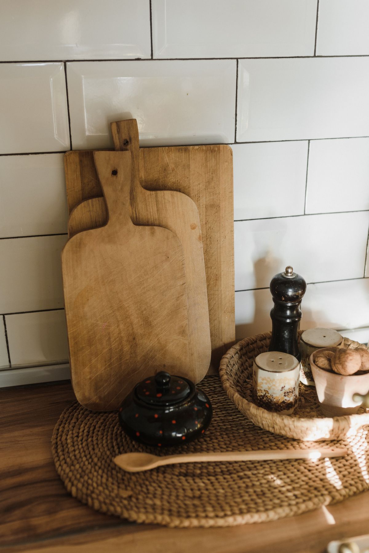 Wooden cutting boards leaning on white tiles beside a pepper mill and a small cup