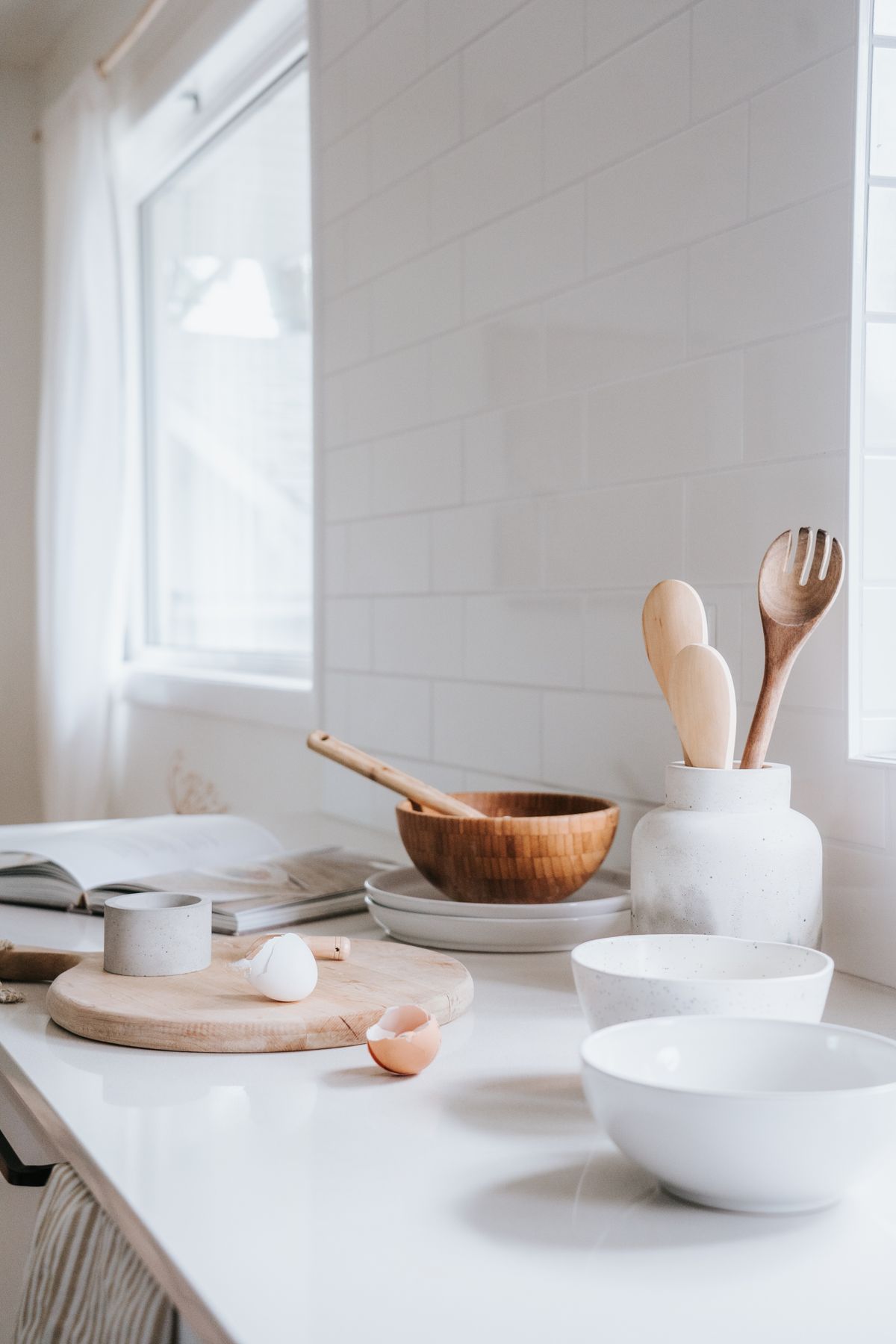 Wooden spoons in a white jar and a wooden bowl on a bright white kitchen counter