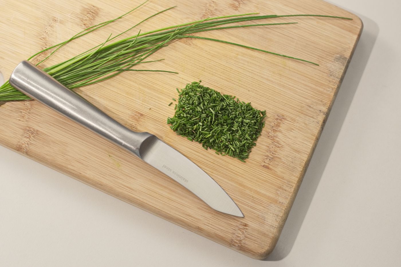 A small steel kitchen knife and chopped chives on a bamboo cutting board