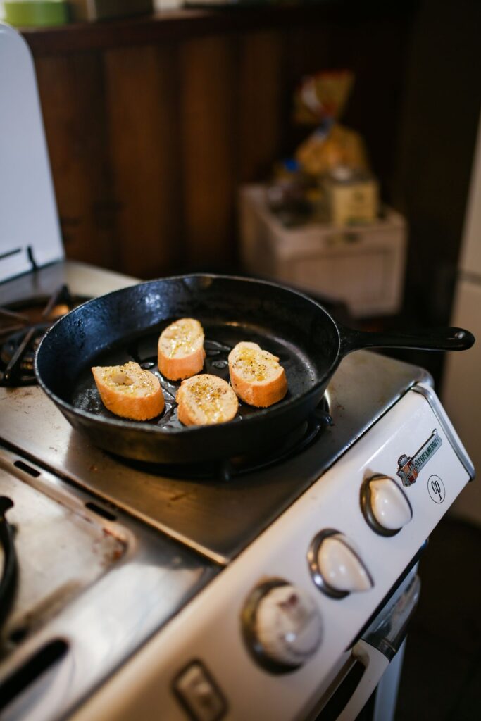 Slices of bread toasting in a cast iron skillet on a small white stove