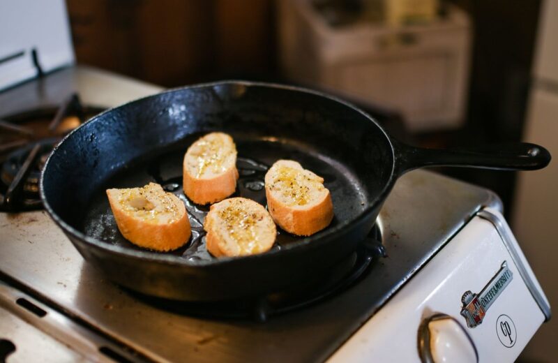 Slices of bread toasting in a cast iron skillet on a small white stove