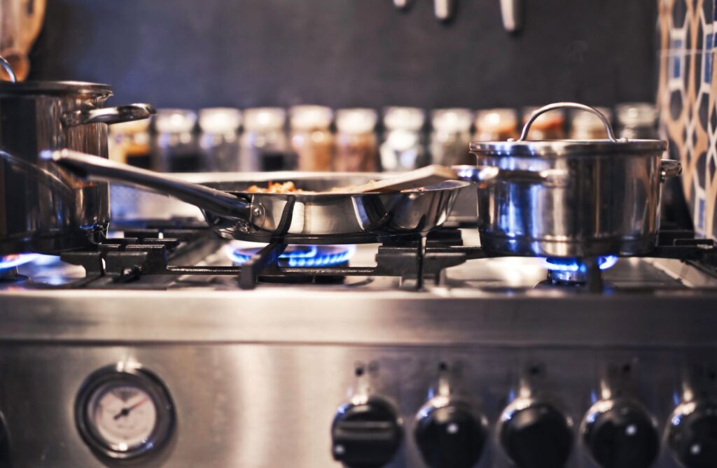 Steel pots and a frying pan on a gas stove with blue flames
