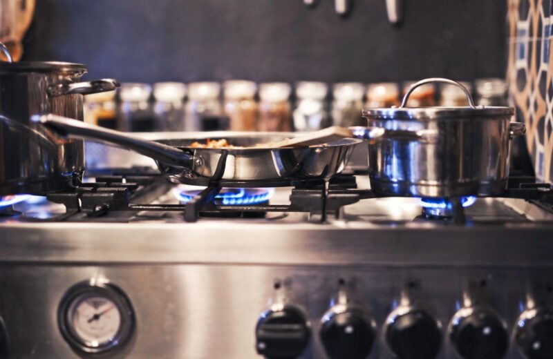 Steel pots and a frying pan on a gas stove with blue flames