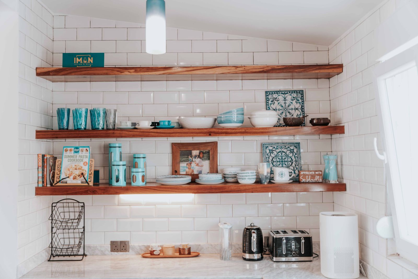 Open wooden shelves on white tiles with plates, mugs, jars and a kettle