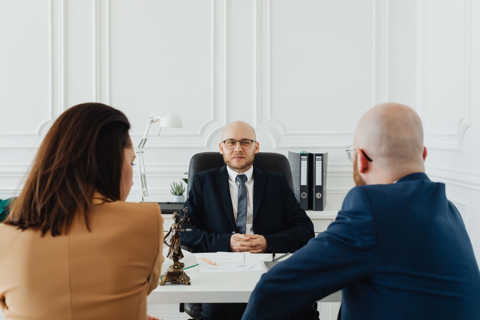 A lawyer at his desk meeting two clients, seen from behind