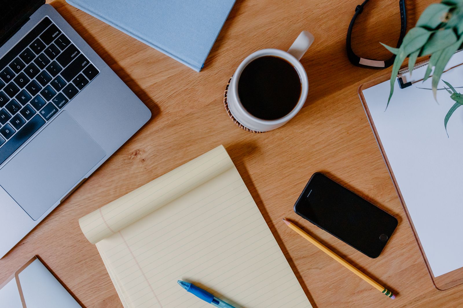A desk from above with a yellow legal pad, a pen, a laptop and a cup of coffee