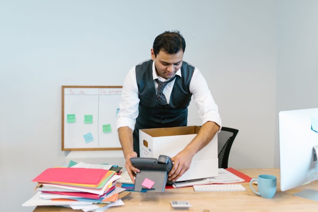 A man packing papers and a phone into a box at his office desk
