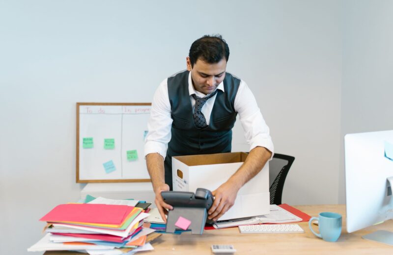 A man packing papers and a phone into a box at his office desk