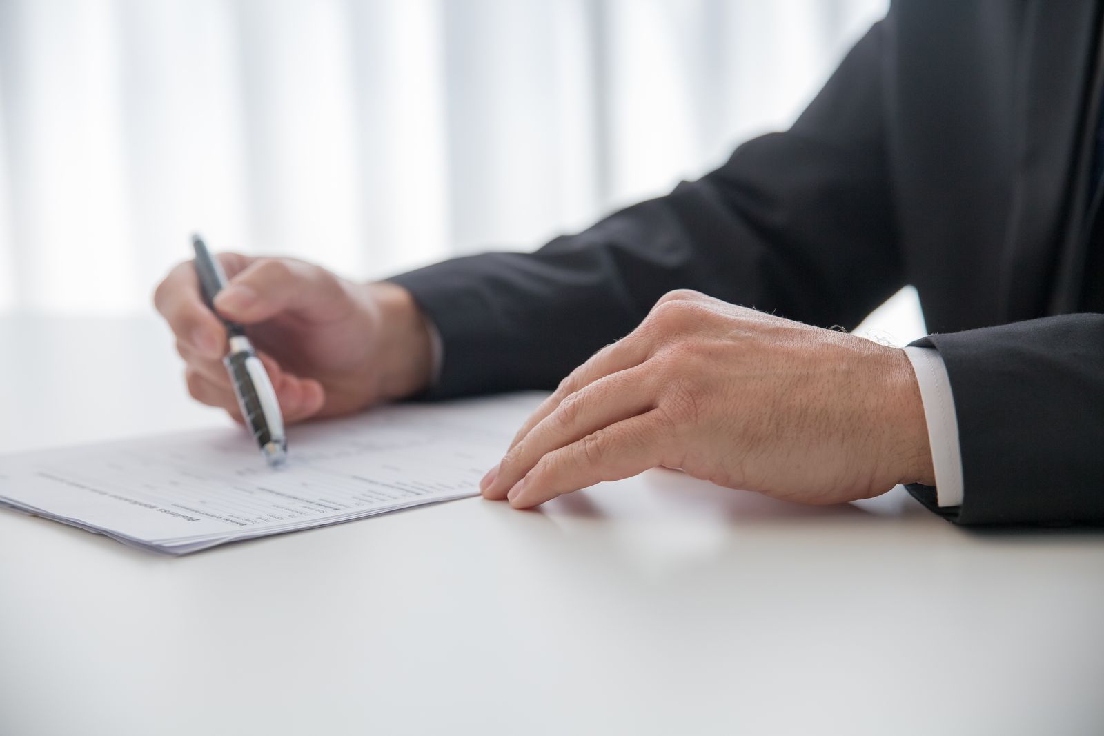 A hand signing a document on a white desk