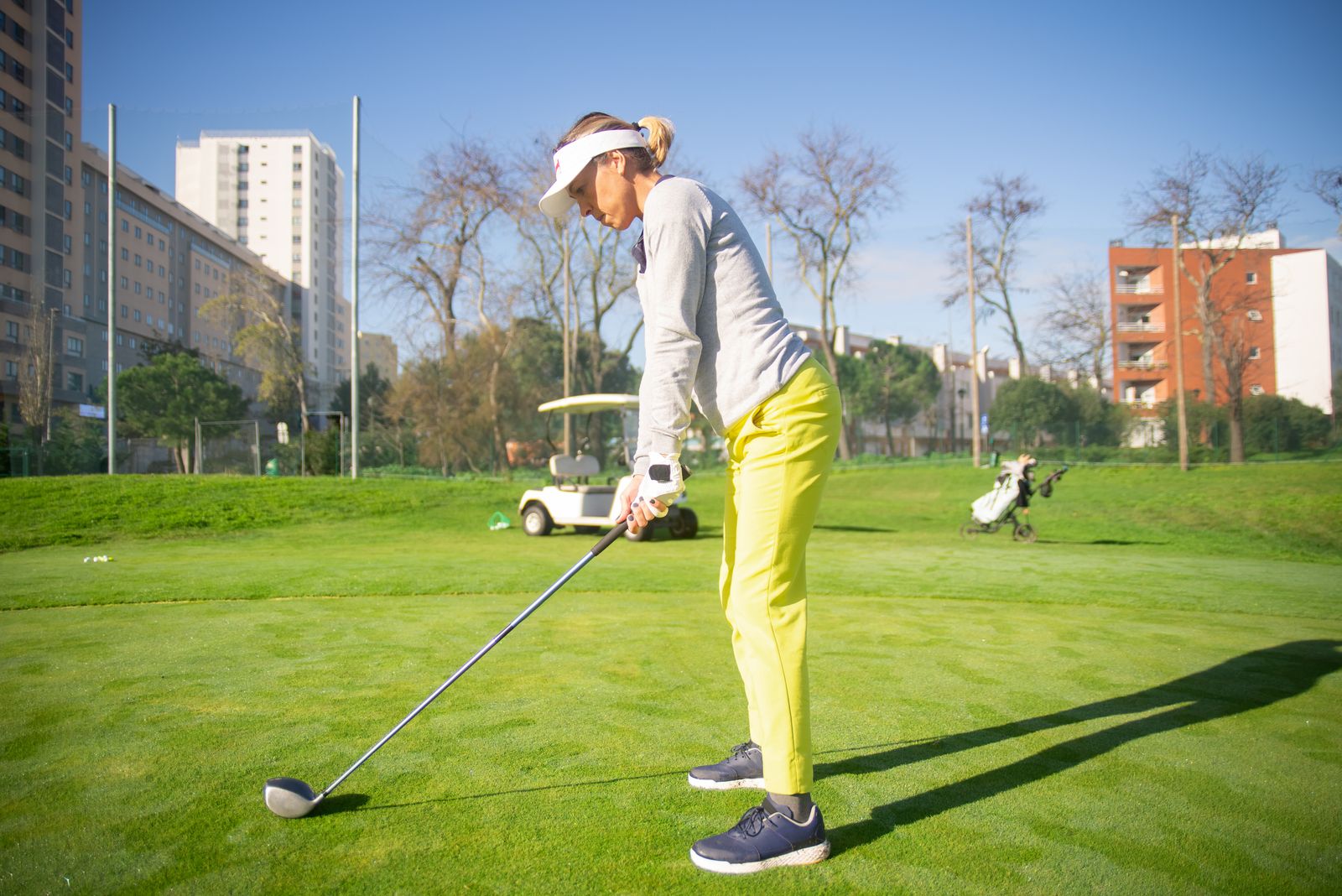 A golfer in a white visor addresses the ball with a driver on a practice ground