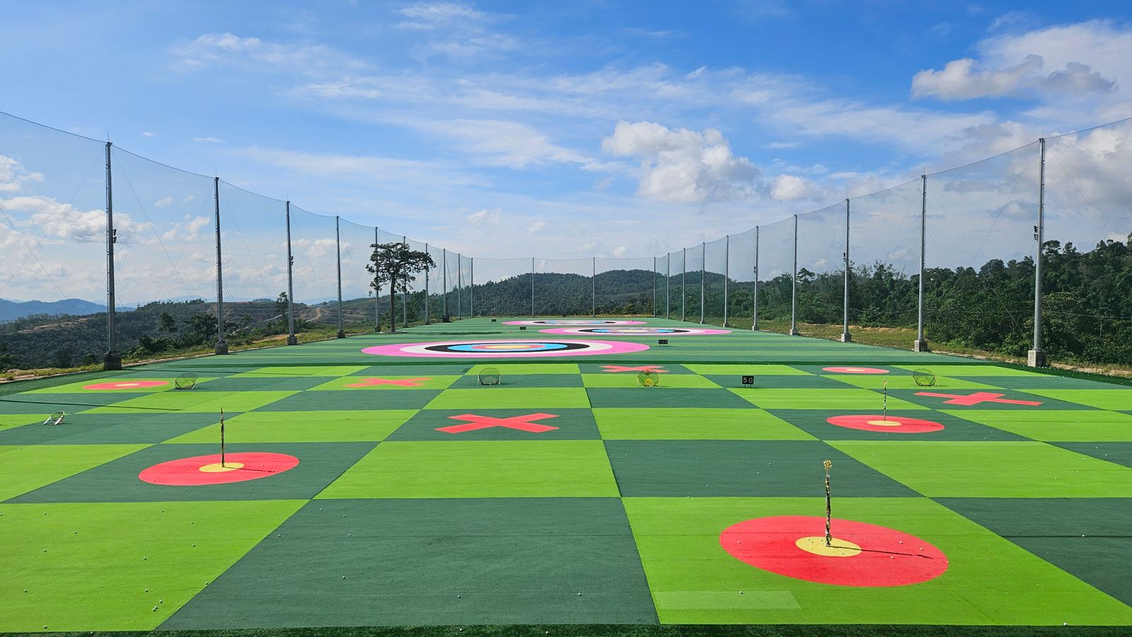 A practice range with round target greens set into the grass and a tall net behind