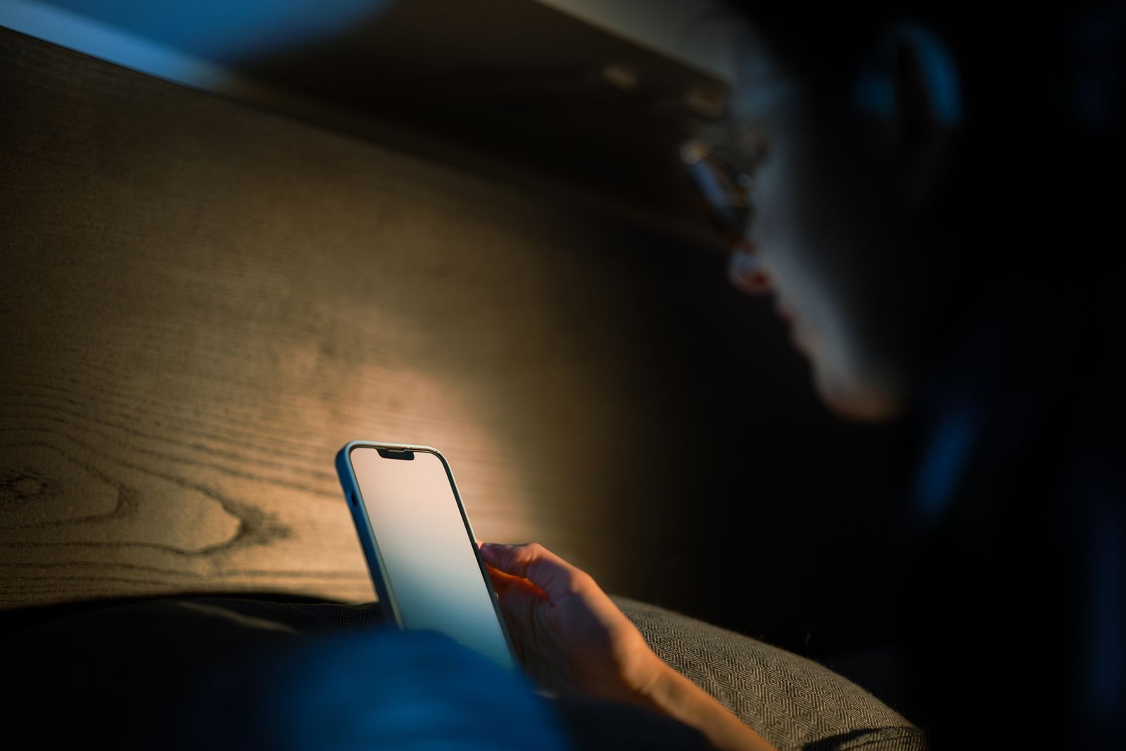 A person reading a phone in a dark room, the screen lighting their hand