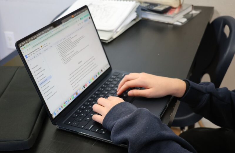 A person typing on a laptop at a desk with papers and books