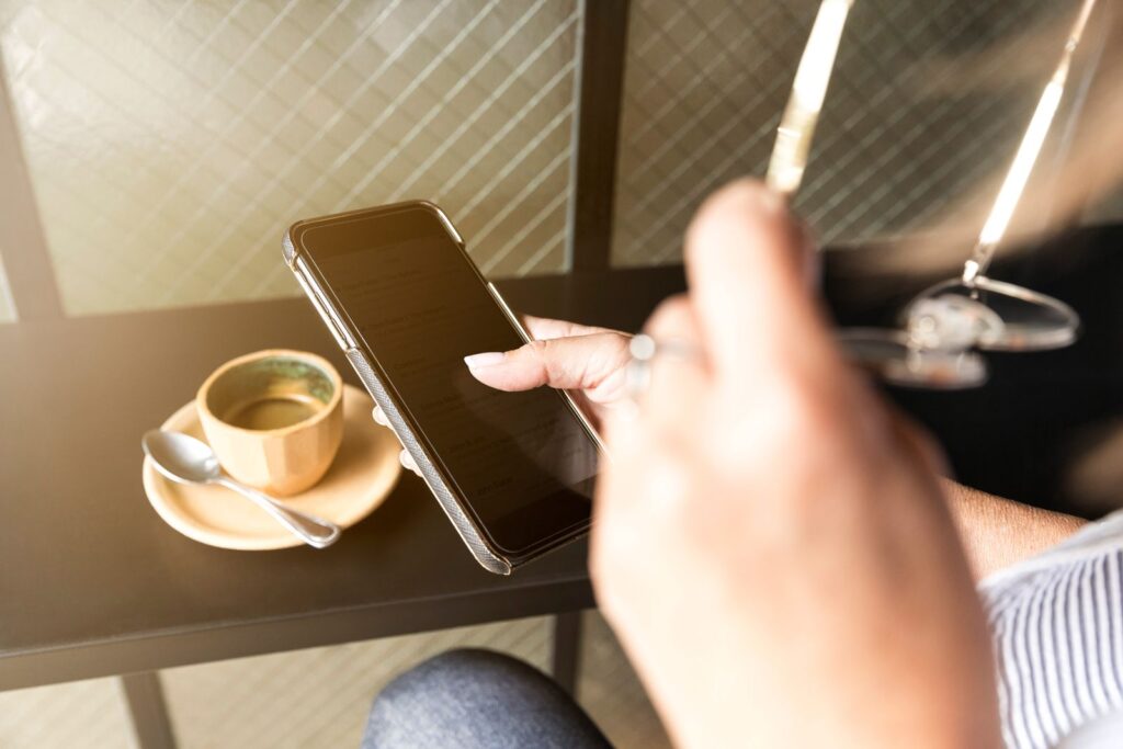 A hand reaching for a phone beside a cup of coffee on a table