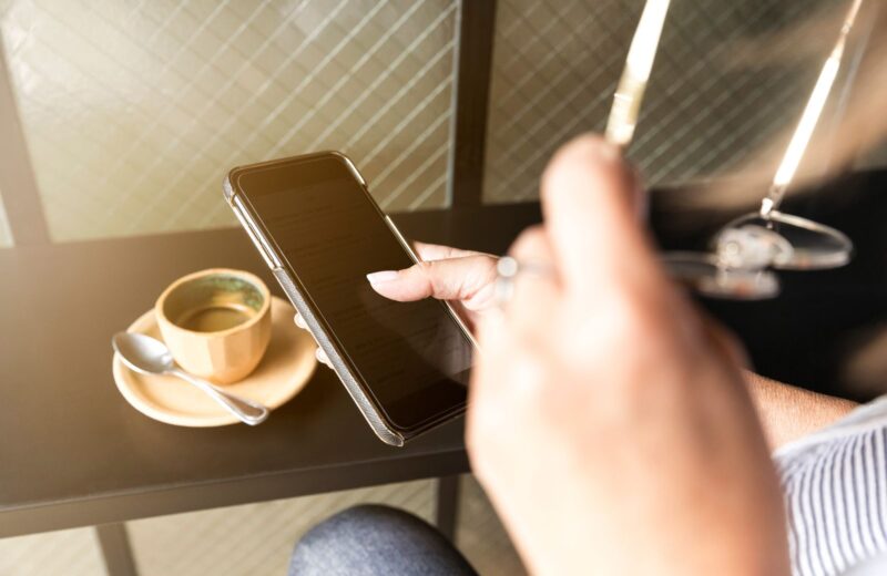 A hand reaching for a phone beside a cup of coffee on a table