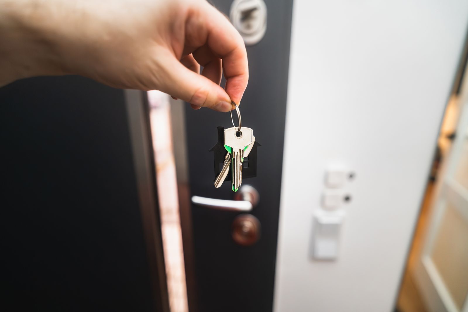 A hand holding a set of house keys in front of an open front door