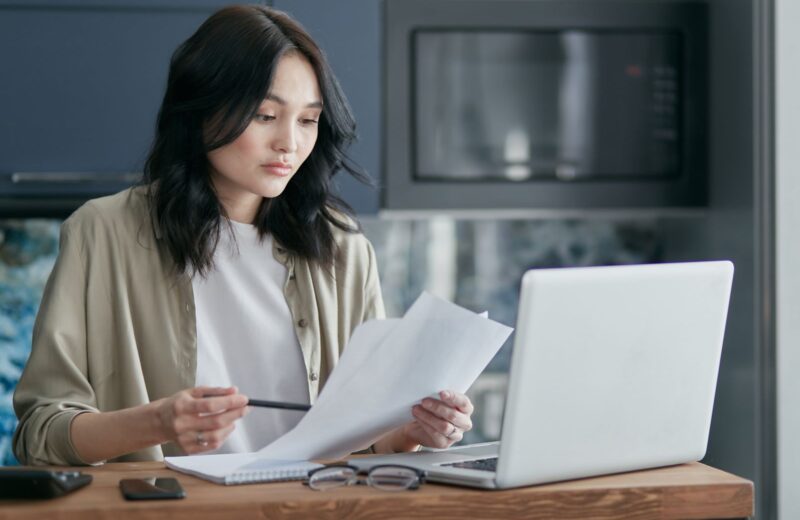 A woman sorting printed documents beside her laptop at home