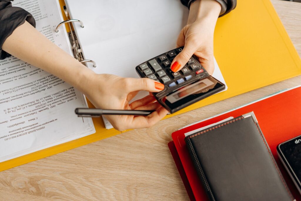 Hands working out figures on a calculator over printed documents and folders