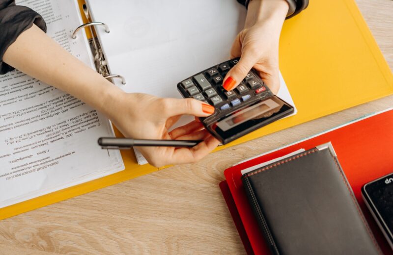 Hands working out figures on a calculator over printed documents and folders