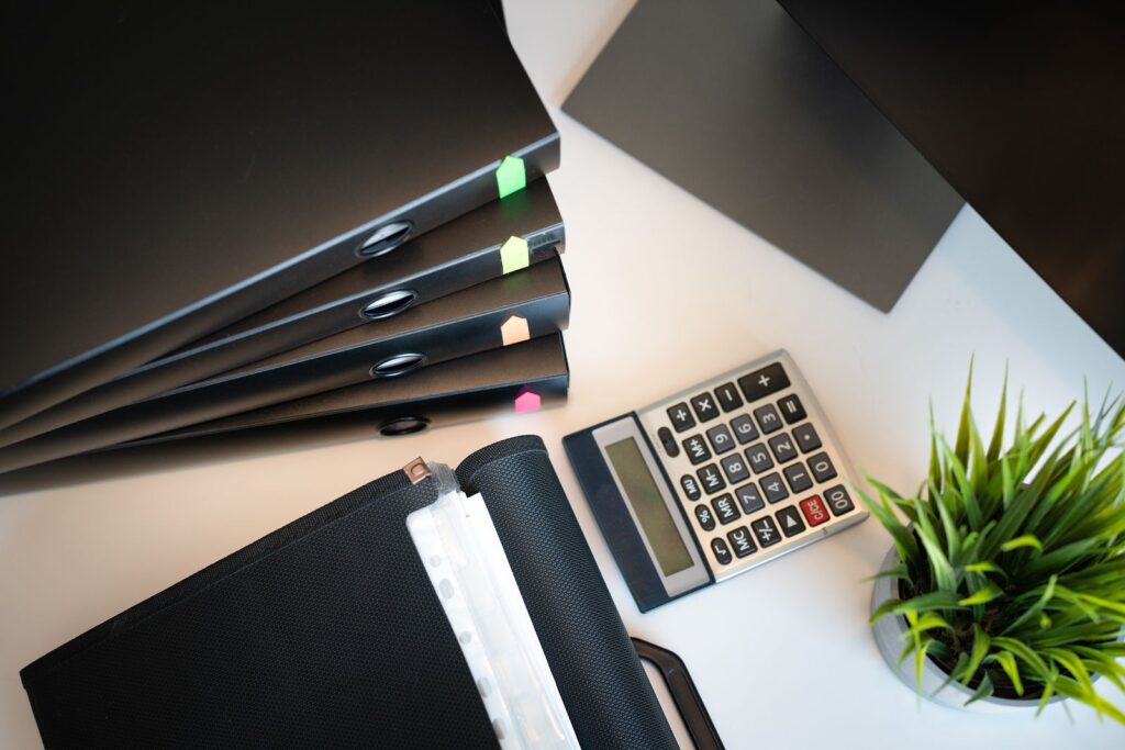 A calculator, reading glasses and black folders on a white desk