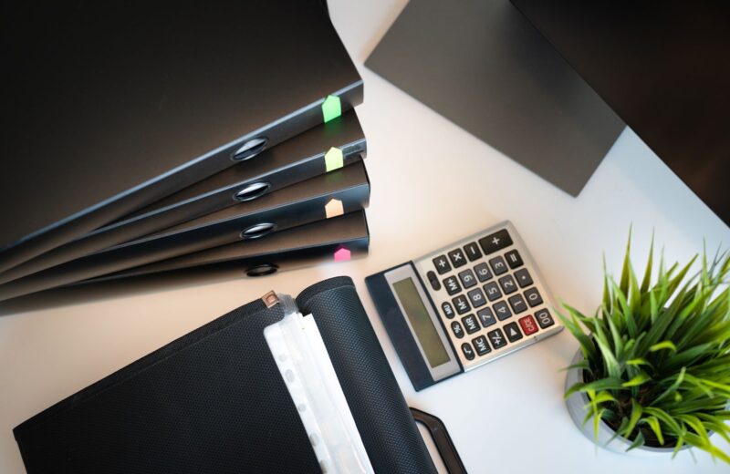 A calculator, reading glasses and black folders on a white desk