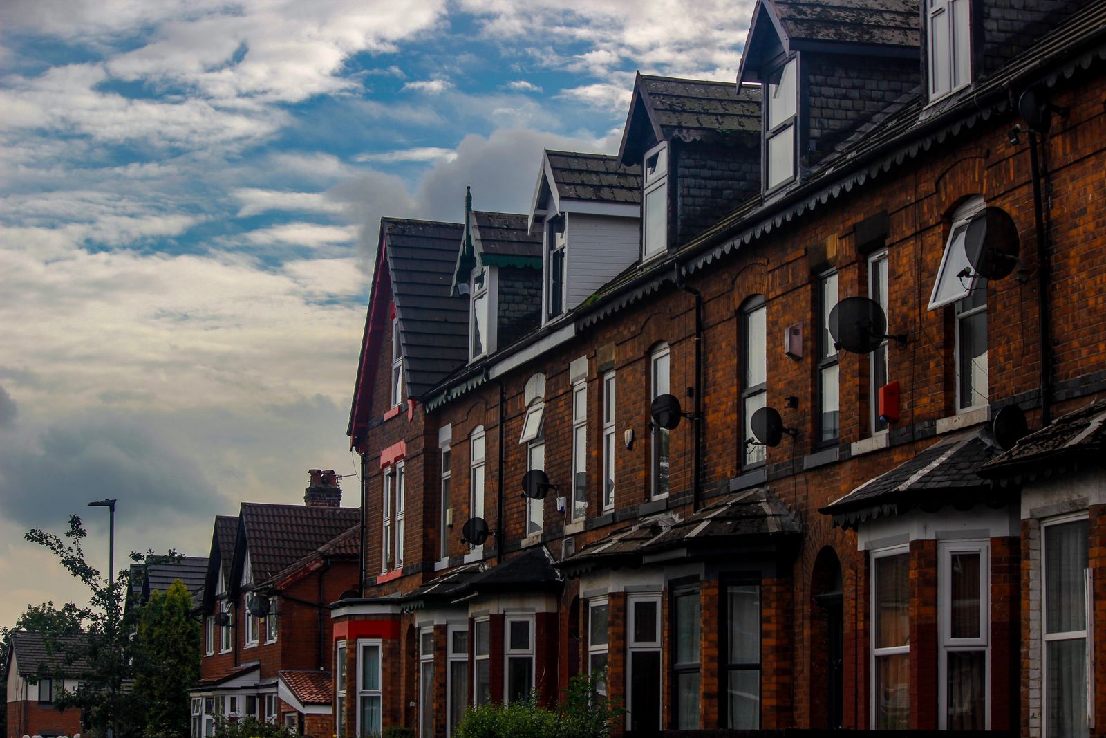 A street of red-brick terraced houses under a cloudy sky