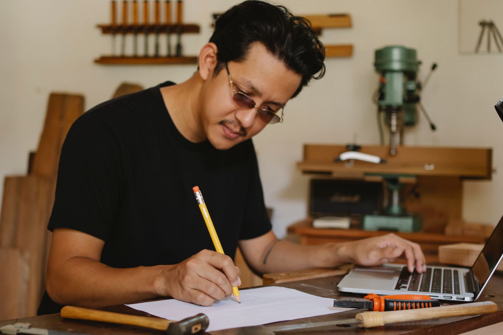 A carpenter writing figures in a notebook beside his laptop in his workshop