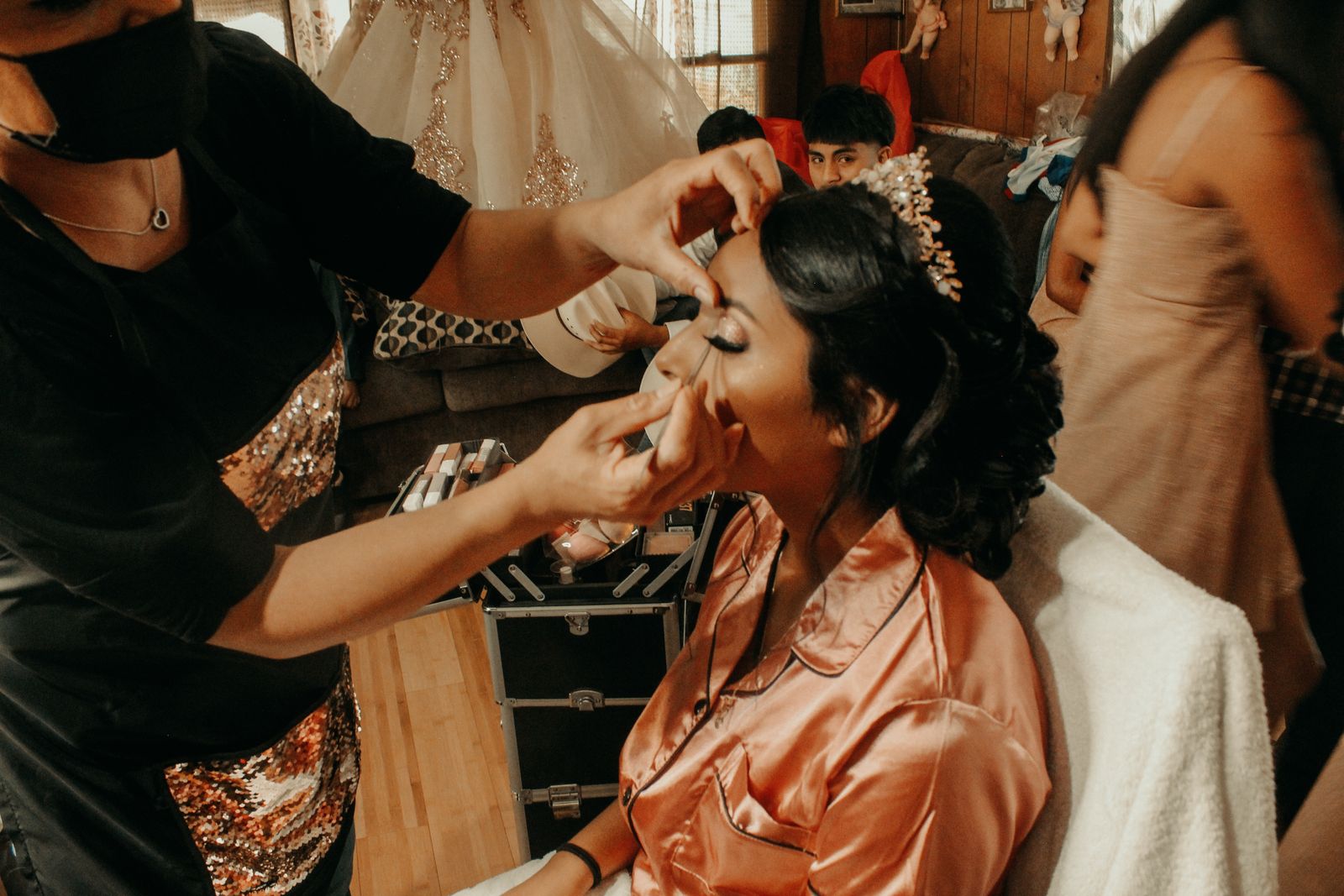 A makeup artist applies eye makeup to a bride in a peach robe before her wedding