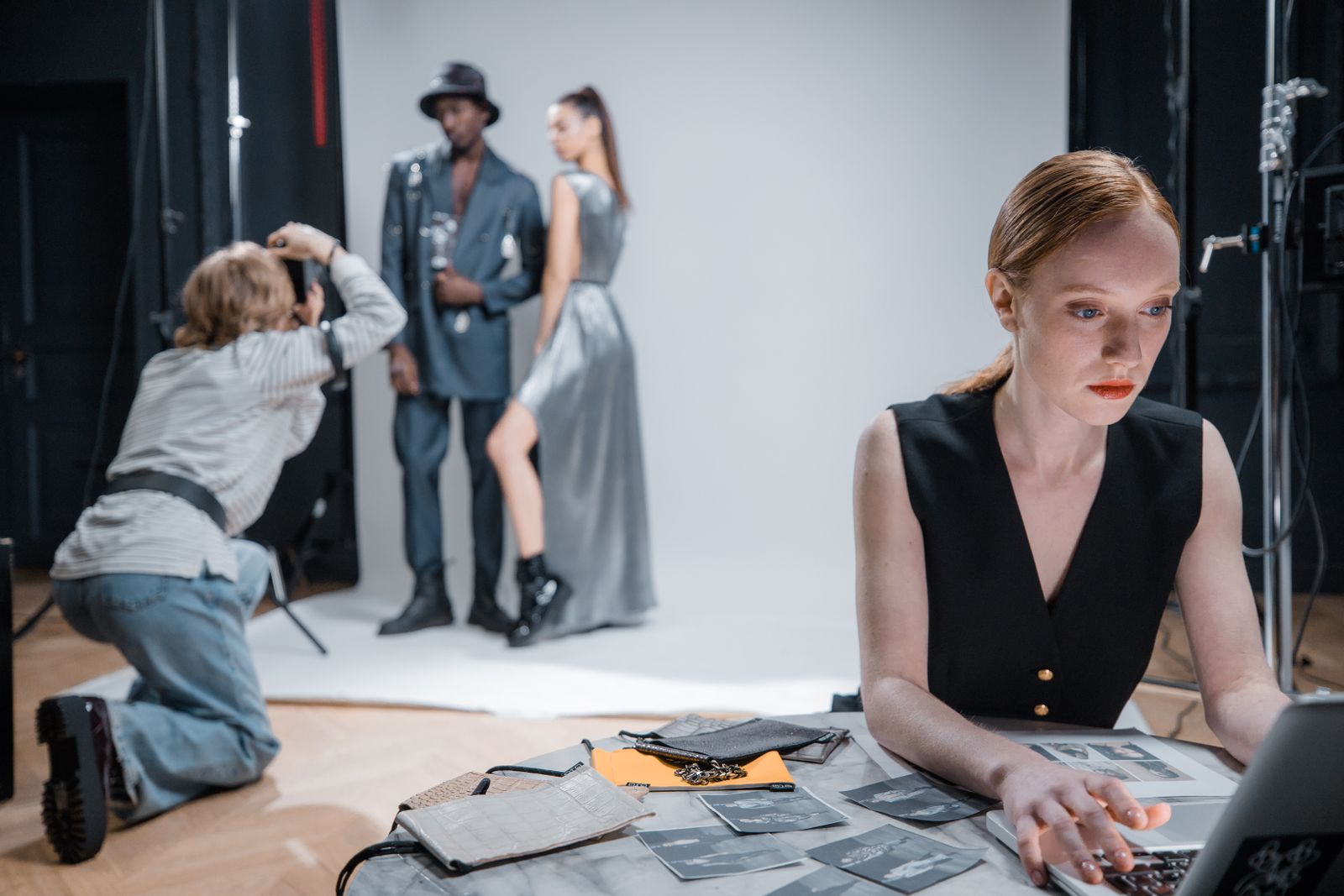 A photographer shoots two models in a white studio while a stylist works at a table