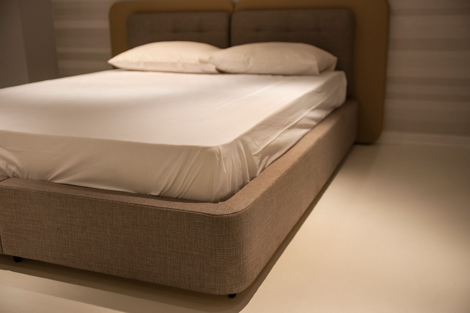 An upholstered bed frame with a padded headboard, made with white sheets and pillows