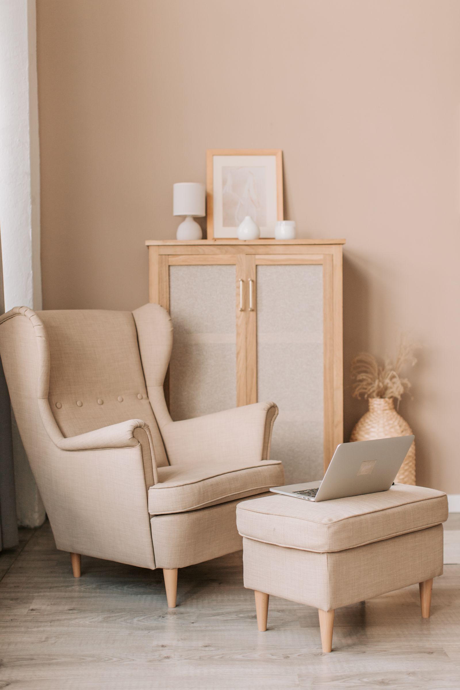 A beige wing armchair with a footstool in a pale room