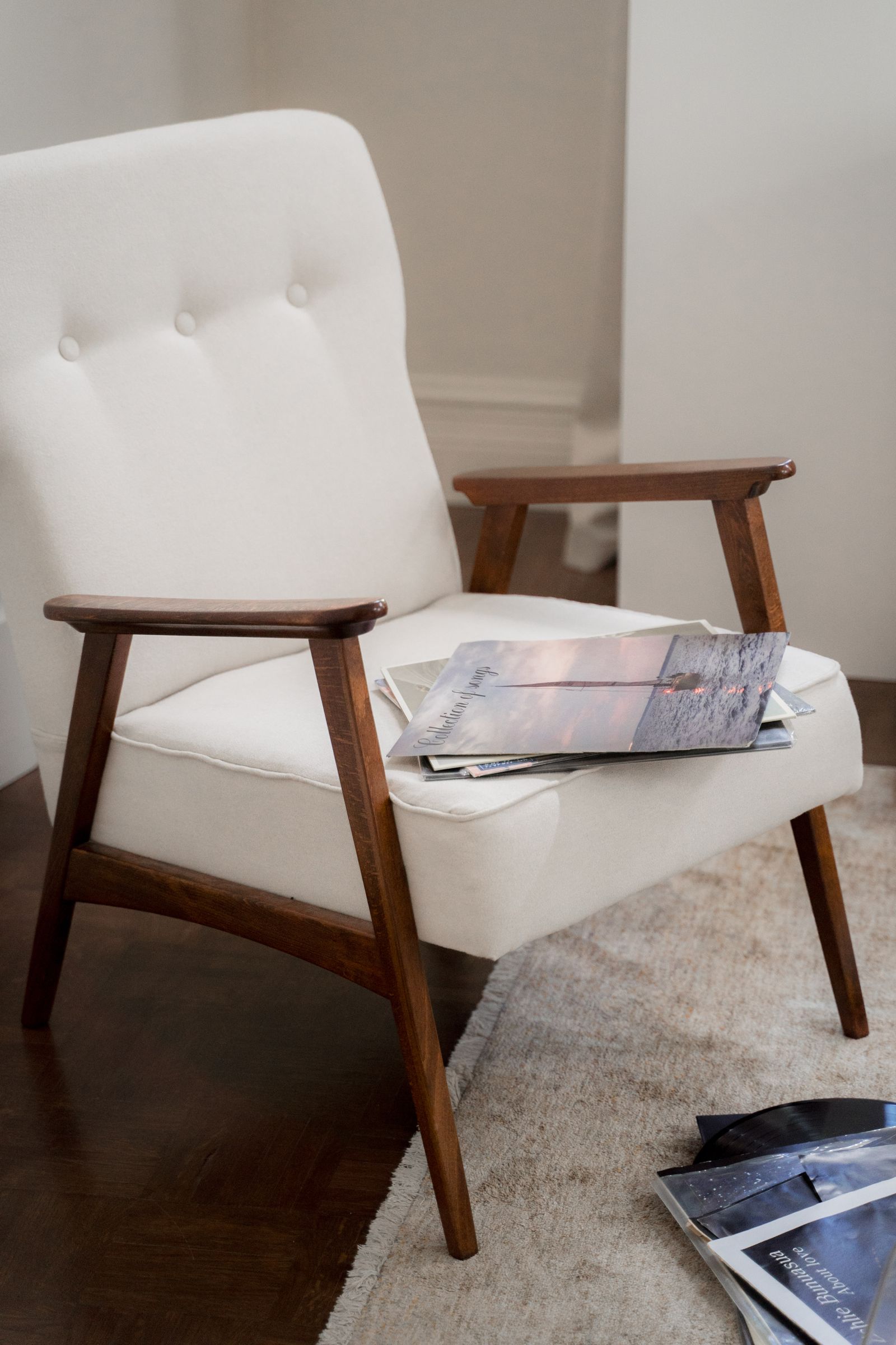 A white upholstered armchair with a wooden frame and a magazine on the seat