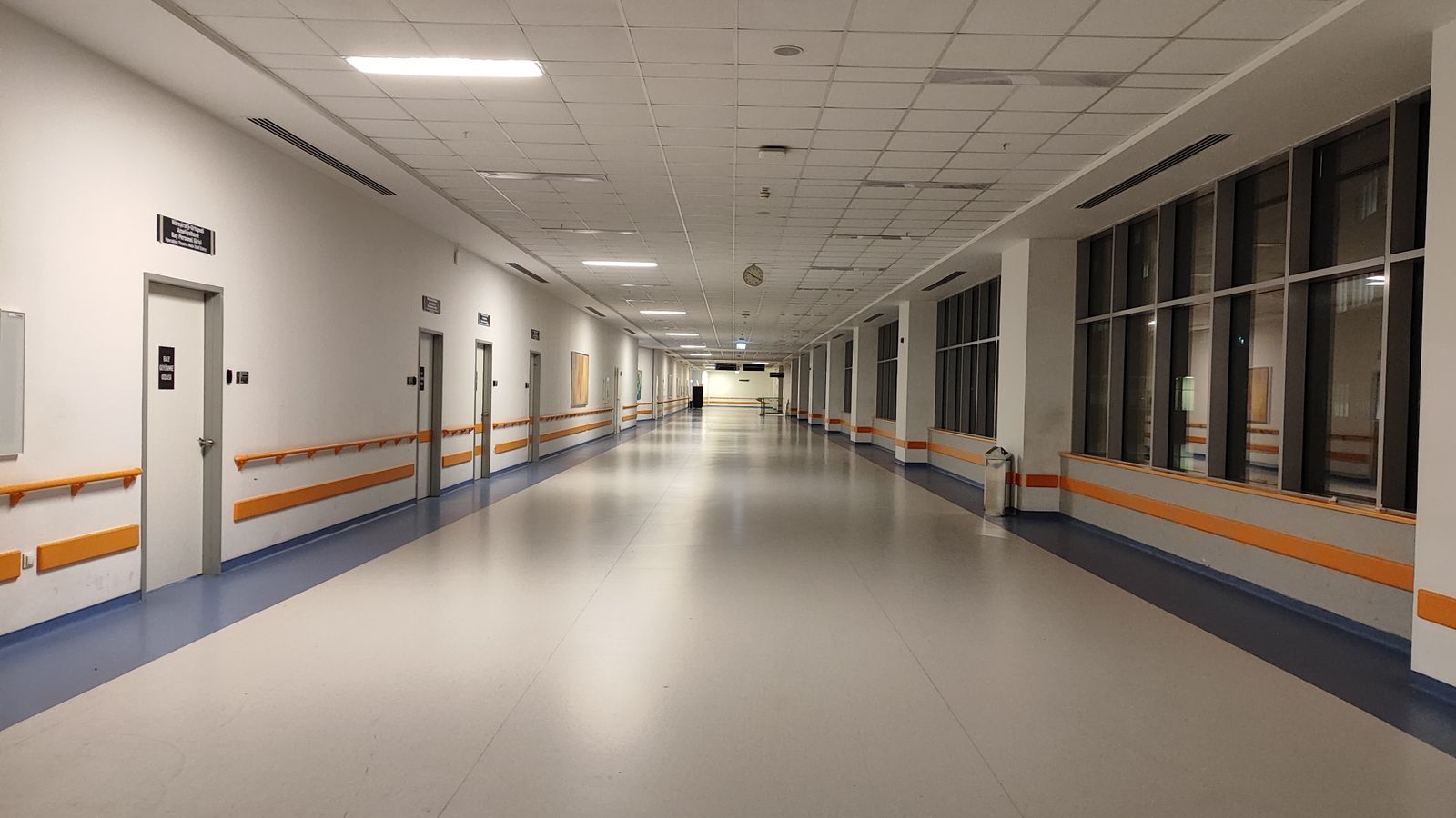 A long, bright hospital corridor with orange guide lines along the wall