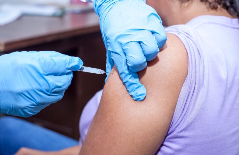A nurse in blue gloves giving a vaccine in an upper arm
