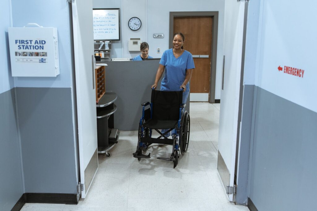 A nurse pushing an empty wheelchair along a hospital corridor