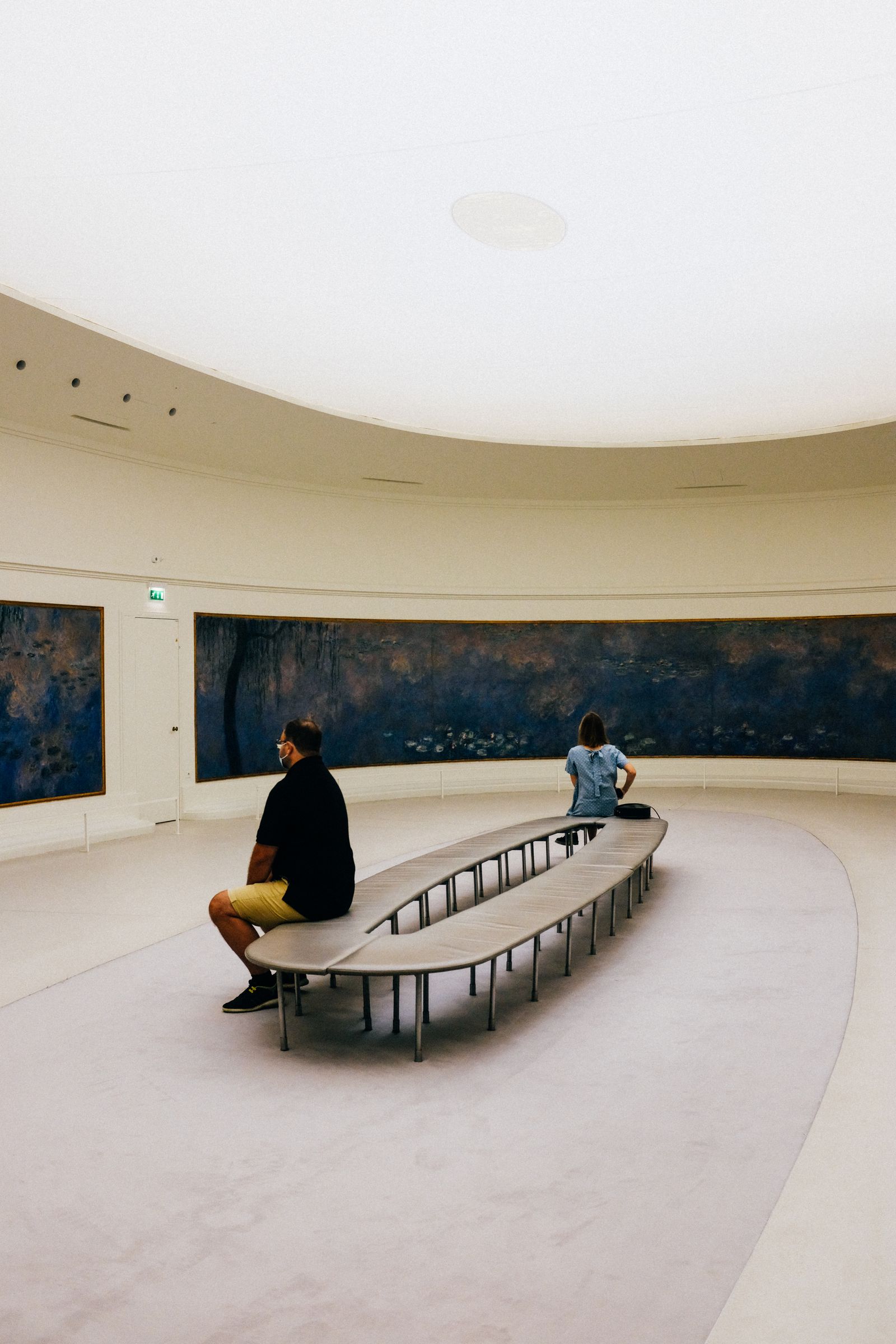 Visitors sitting in a round gallery hung with large paintings