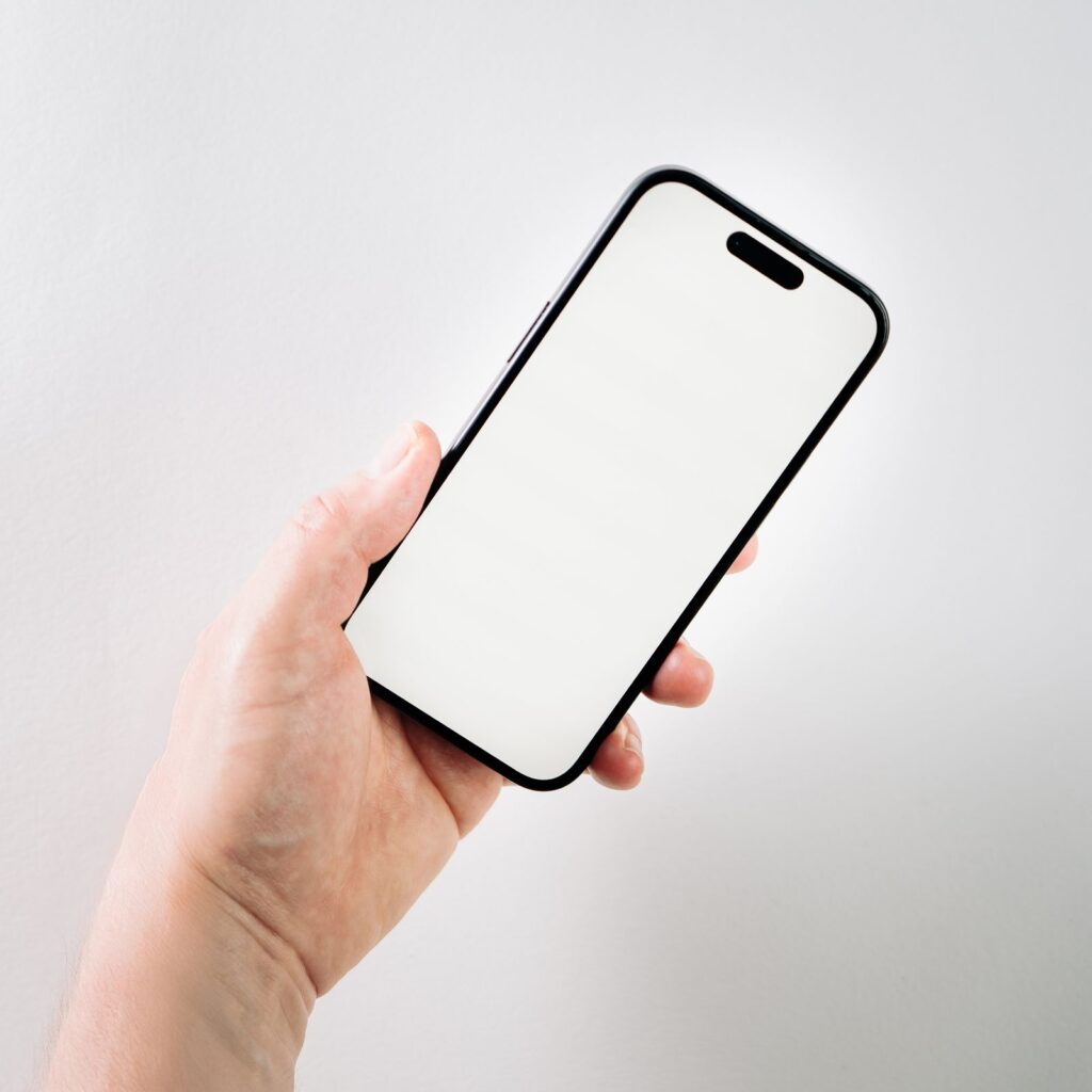 A hand holding a phone with a blank white screen against a pale wall