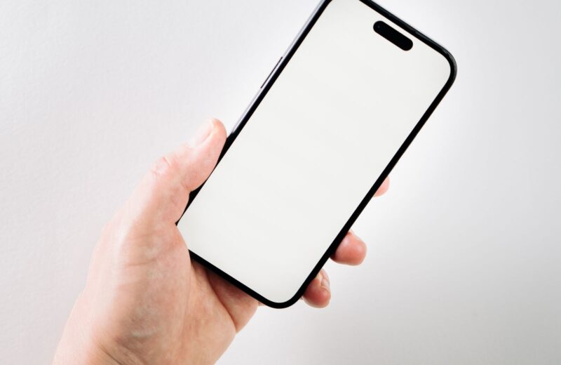 A hand holding a phone with a blank white screen against a pale wall