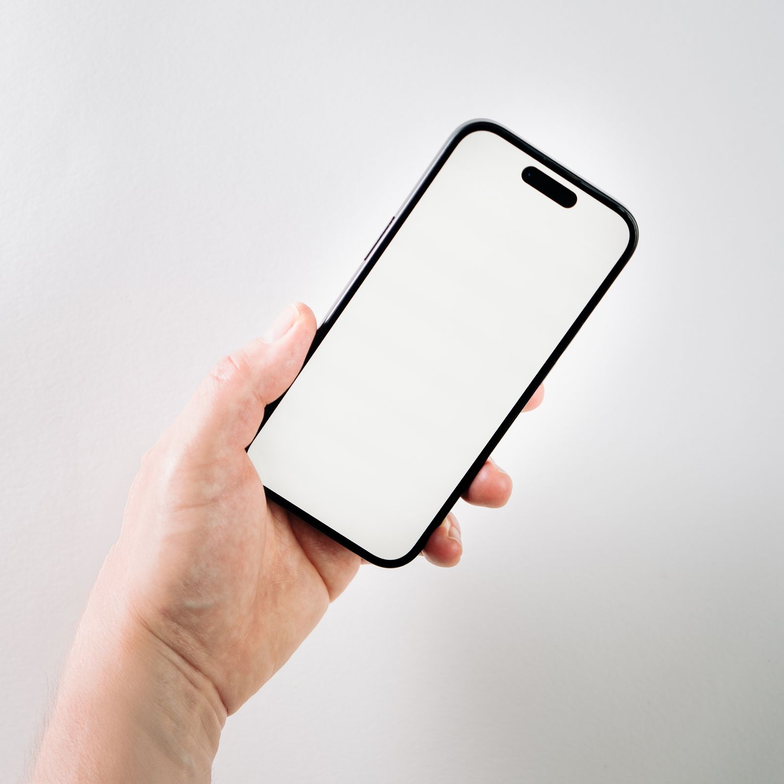 A hand holding a phone with a blank white screen against a pale wall