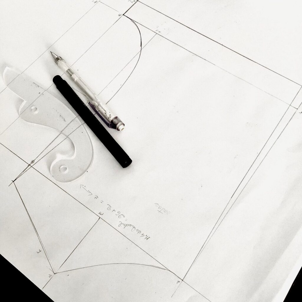 Pencil layout lines on white paper with a French curve and two pens