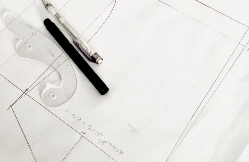 Pencil layout lines on white paper with a French curve and two pens