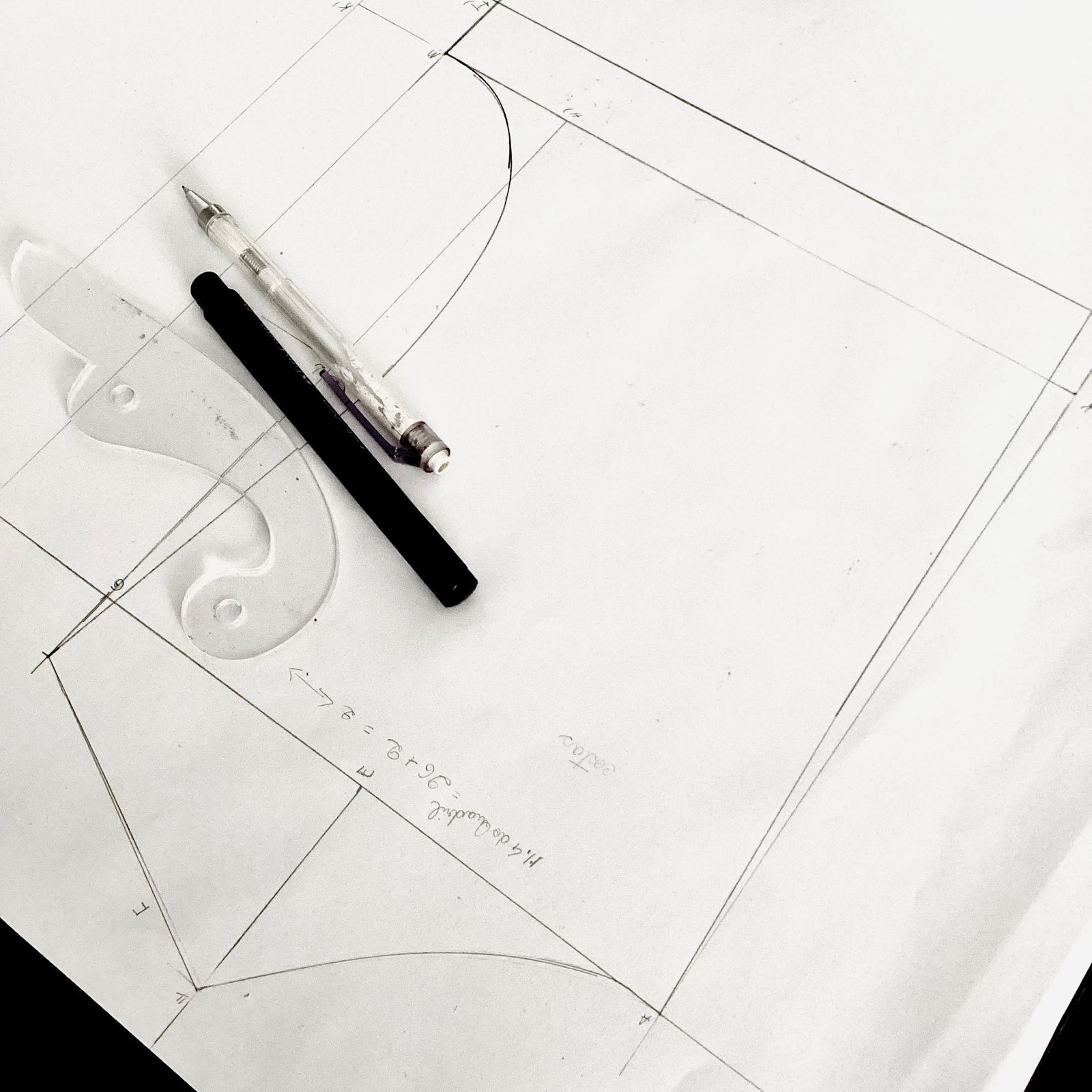 Pencil layout lines on white paper with a French curve and two pens