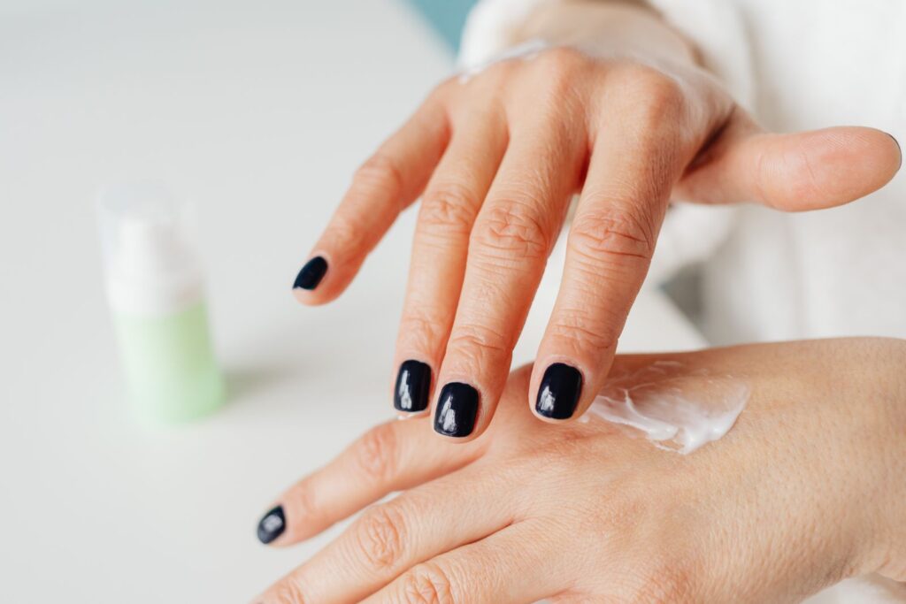 Hands with dark nails rubbing in hand cream