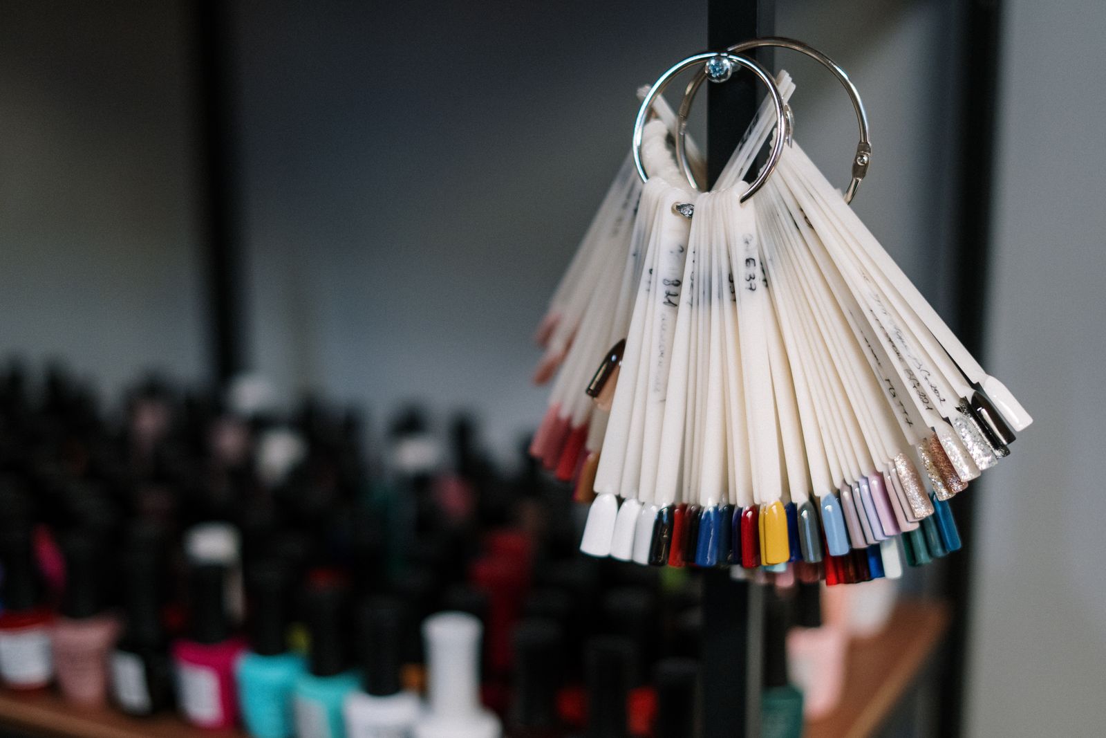 A ring of painted nail tips held up in front of a wall of polish bottles