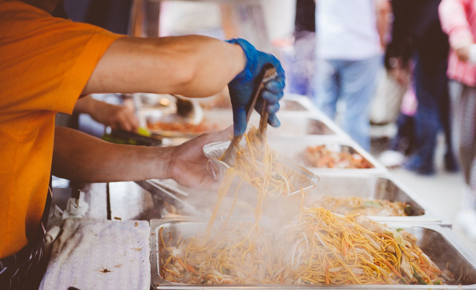 A street cook tossing noodles in a pan at a market stall